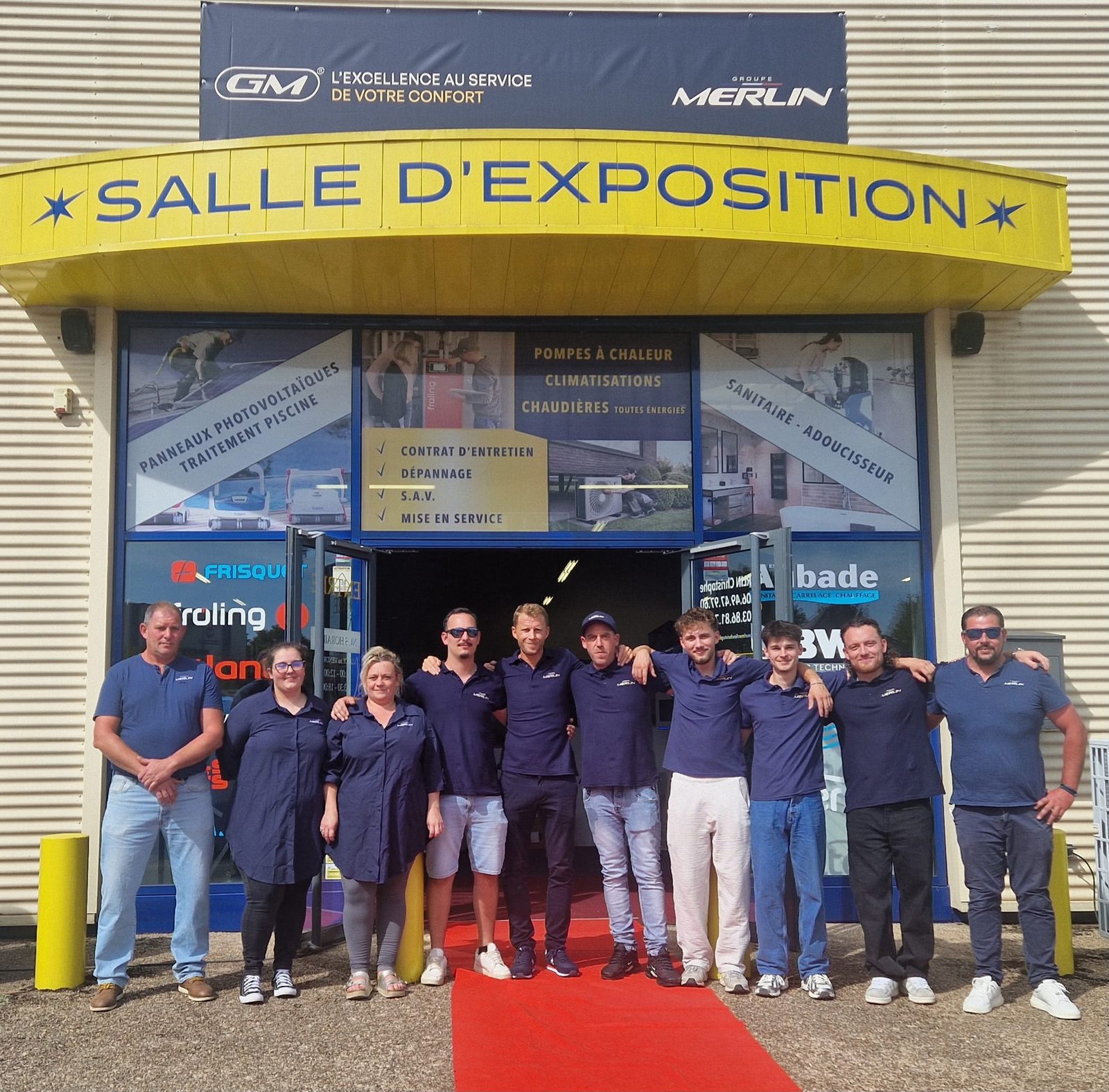 Onze membres de l'équipe du Groupe Merlin, en polo bleu marine, posent sur le tapis rouge devant le showroom de Clamecy